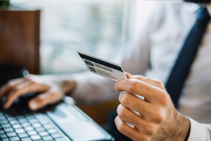 Business man holding credit card in hand while using laptop